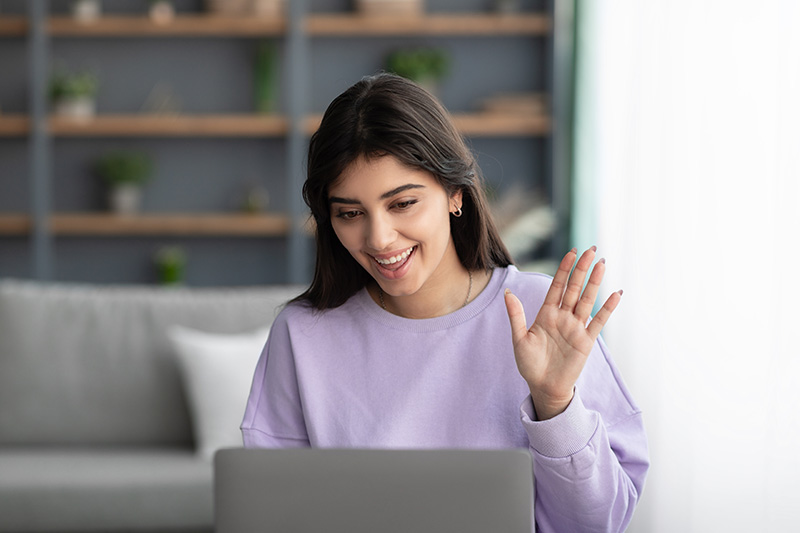 A woman waves at her computer's camera while participating in a virtual IOP program.