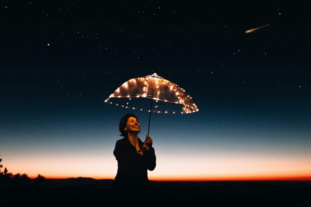 Woman holds an umbrella in the evening with lights in it showing how recovery rewires the brain helping you feel happier.